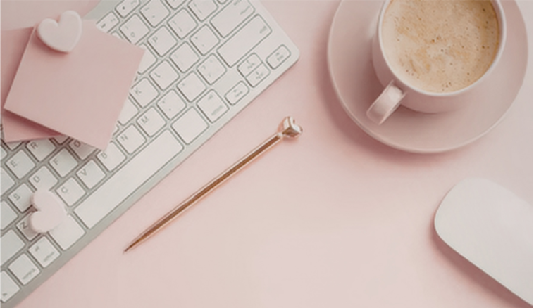 A pink workspace with a keyboard, a white mouse, a cup of coffee, a pink sticky note with heart decorations, and a decorative pin.