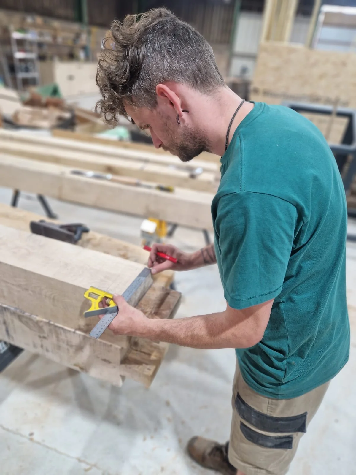 Carpenter measuring and marking timber with a square and red marker in the Cabins & Wagons workshop in Devon.