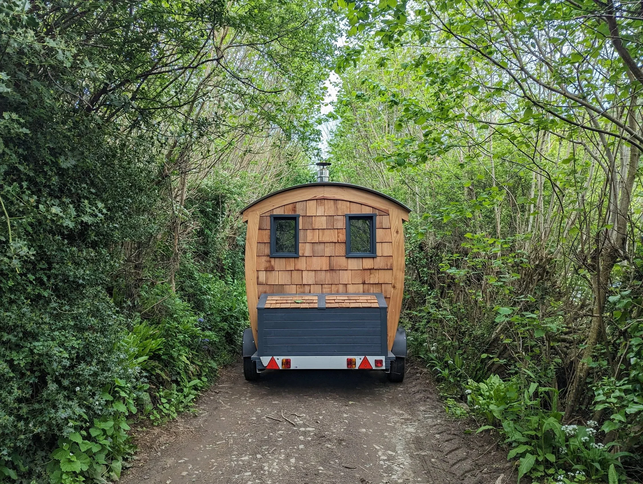 Mobile cedar-clad sauna on a trailer being towed along a Devon lane, handcrafted by Cabins & Wagons.