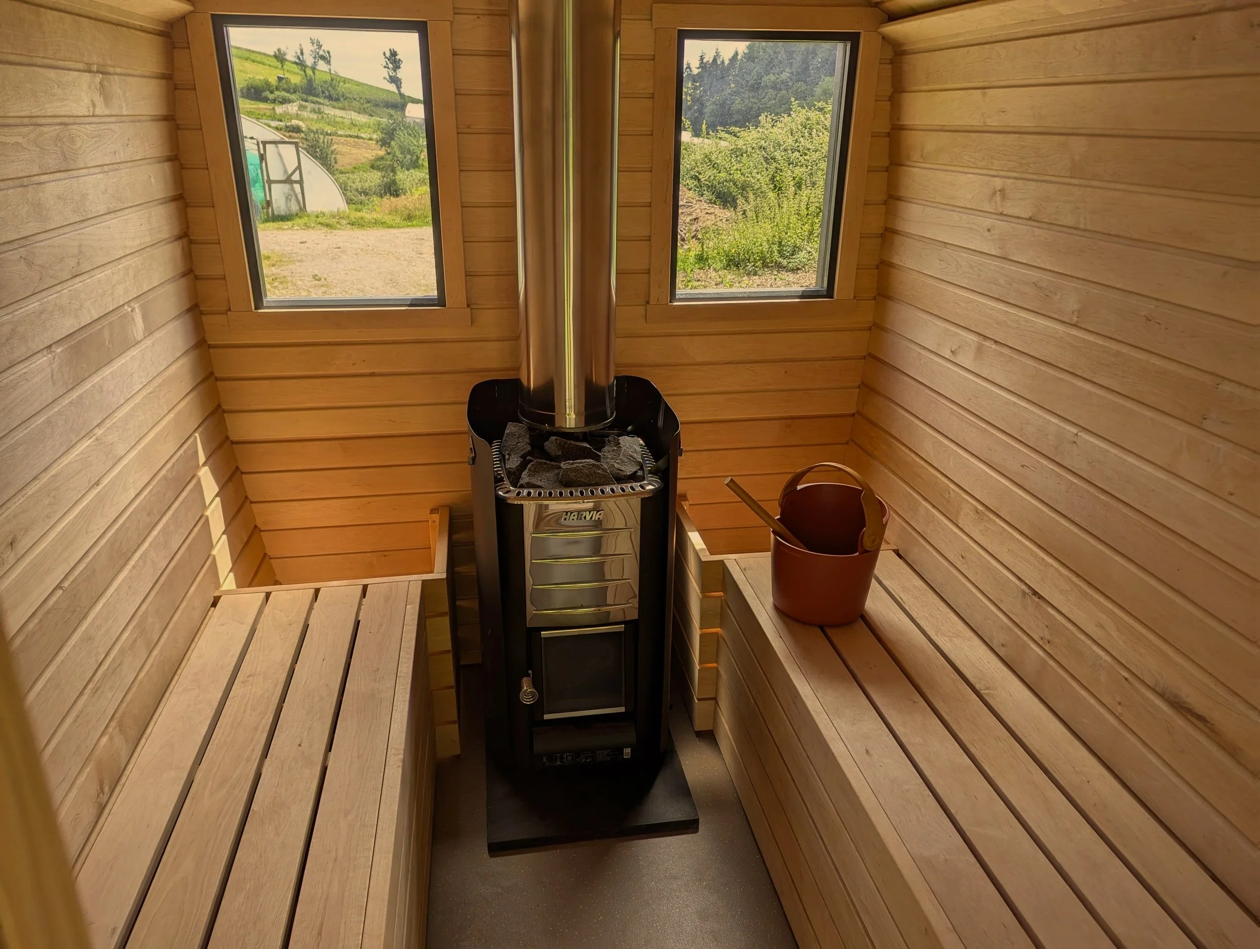 Interior of a handcrafted sauna with wood-burning stove, benches and windows, built in Devon by Cabins & Wagons.