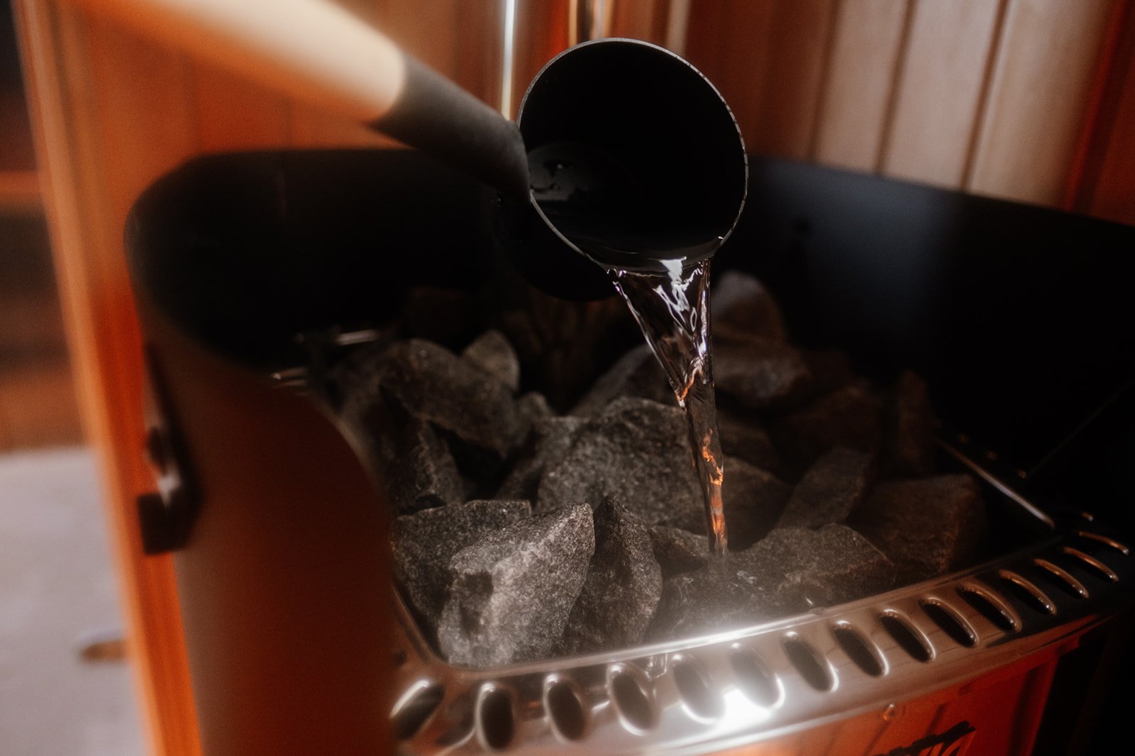Person pouring water onto hot sauna stones during a group sauna session