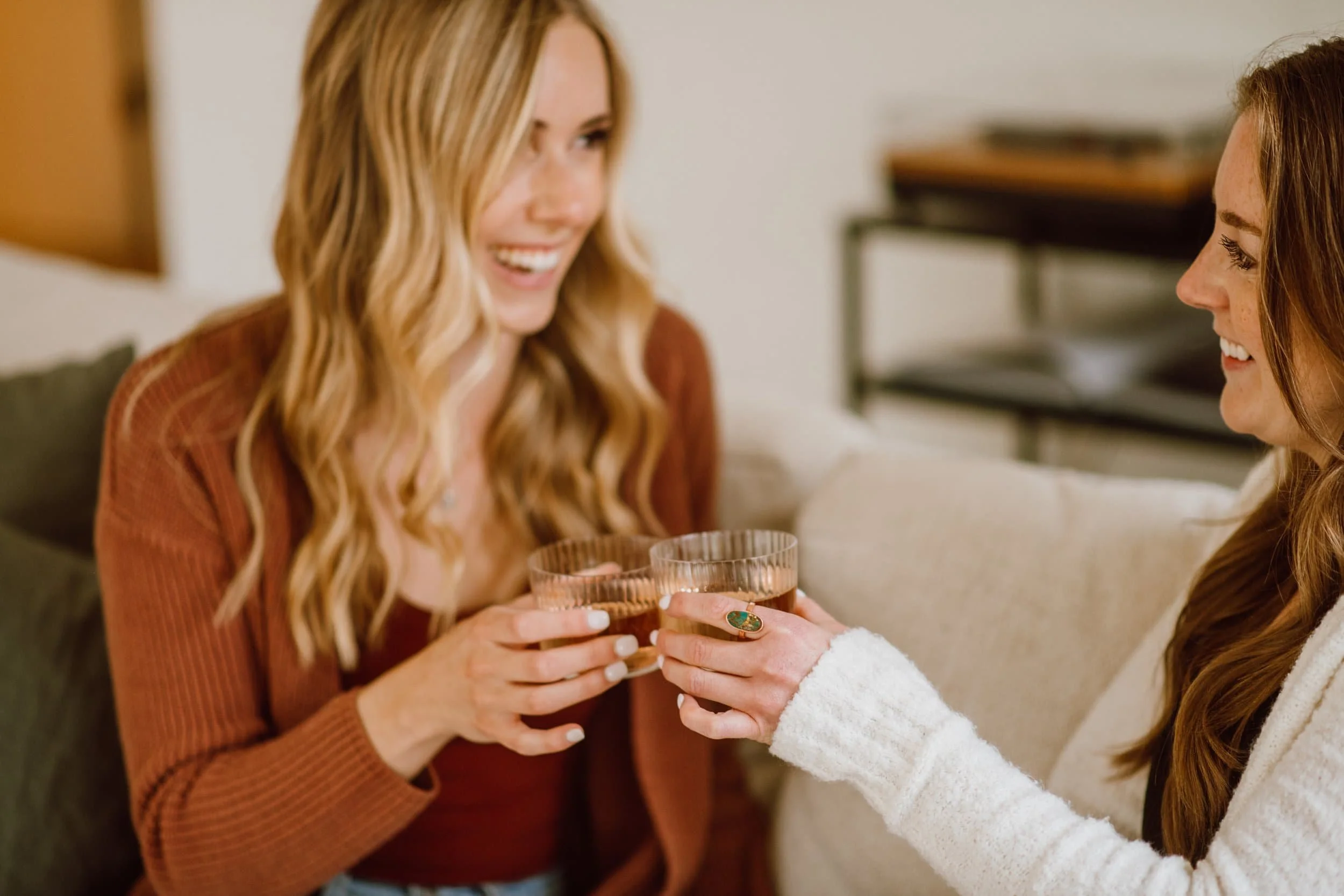 Two women sharing a toast with glasses of drinks during a friendly gathering.