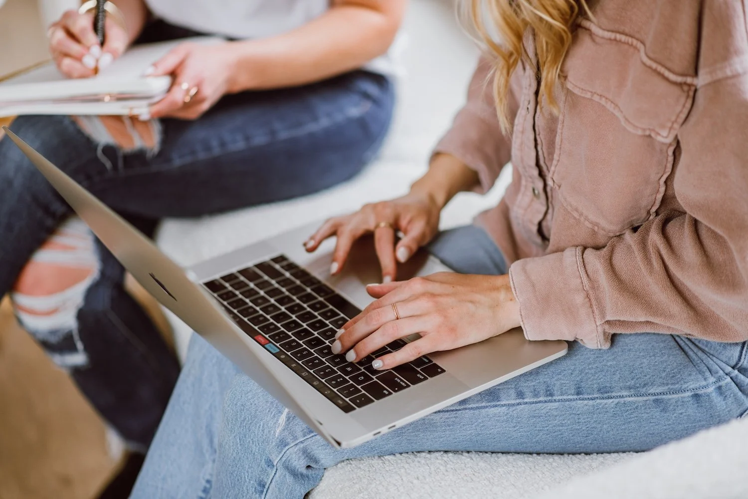 Woman in pink shirt and jeans typing on computer.