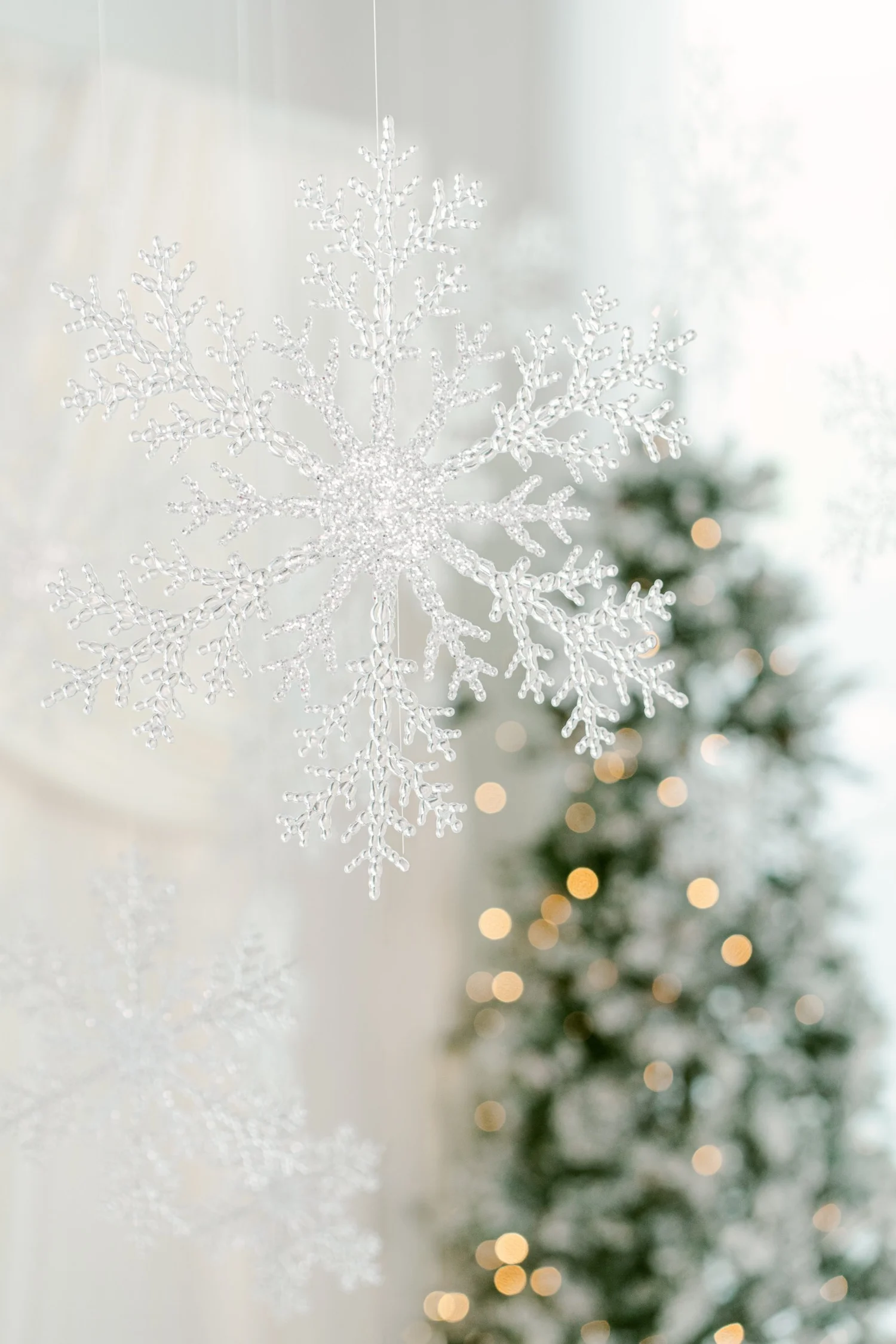 Oversized glitter snowflake hanging in front of ivory drapes and a lit frosted tree on the Winter White holiday photo set in Pflugerville