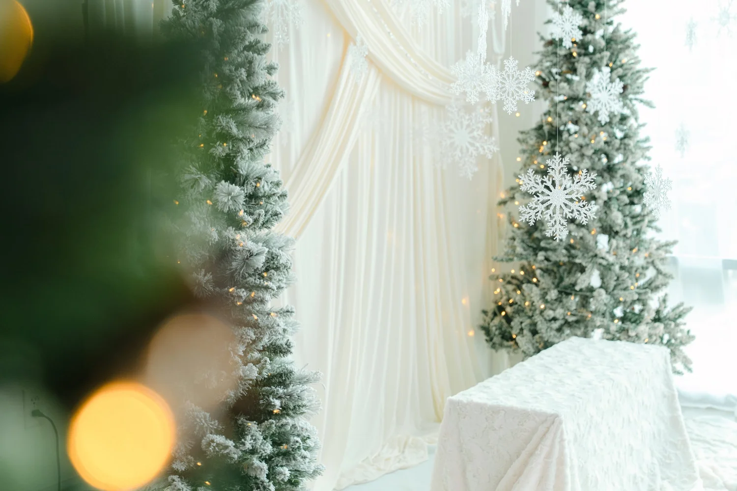 Frosted Christmas trees, hanging snowflakes and a faux fur bench against ivory drapes on the Winter White holiday photo set in North Austin