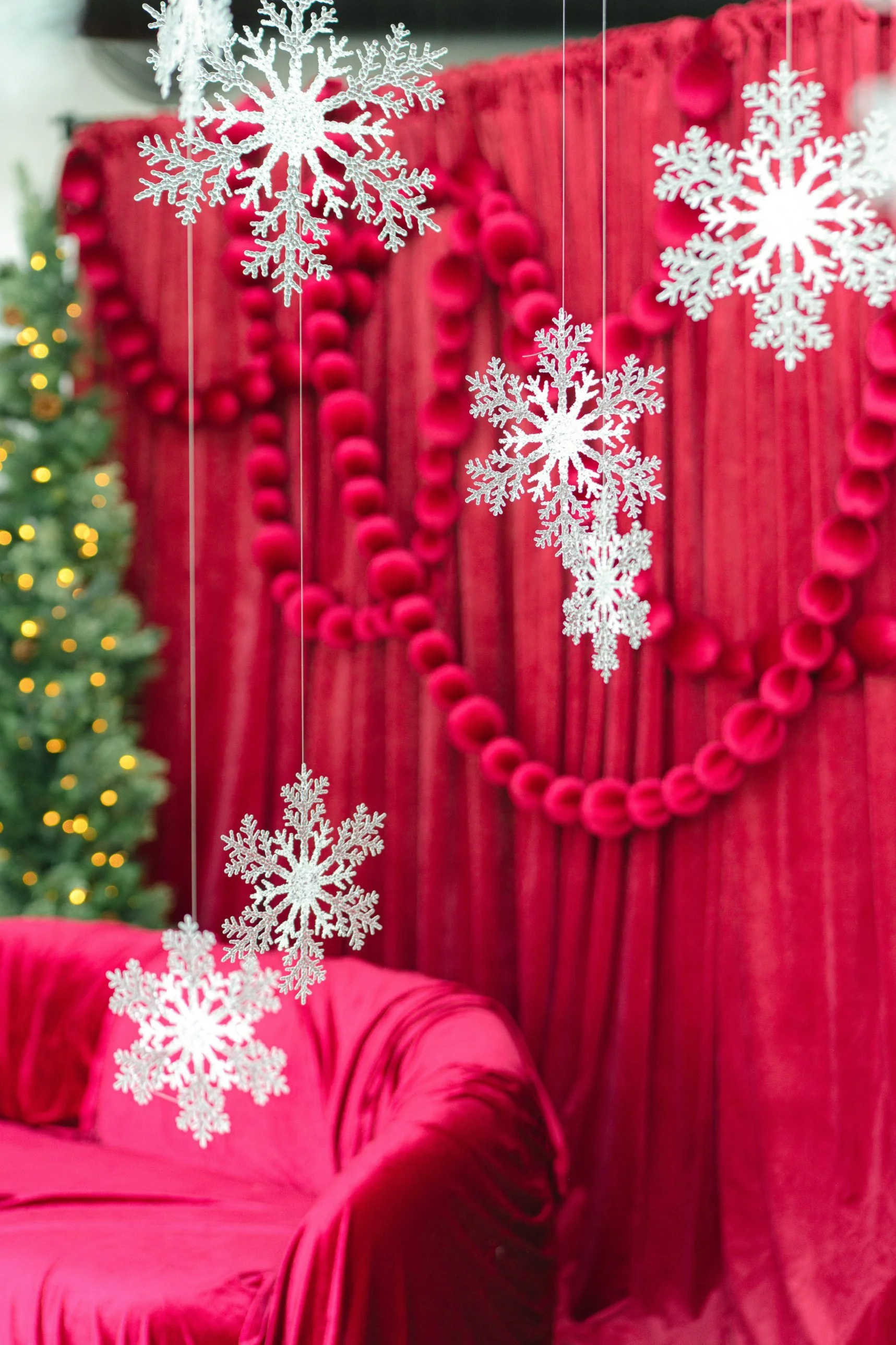 Glitter snowflakes from the Winter White set floating in front of the cranberry velvet drape and loveseat on the Red Velvet holiday photo set at Alight Collaborative in Pflugerville, near Austin TX