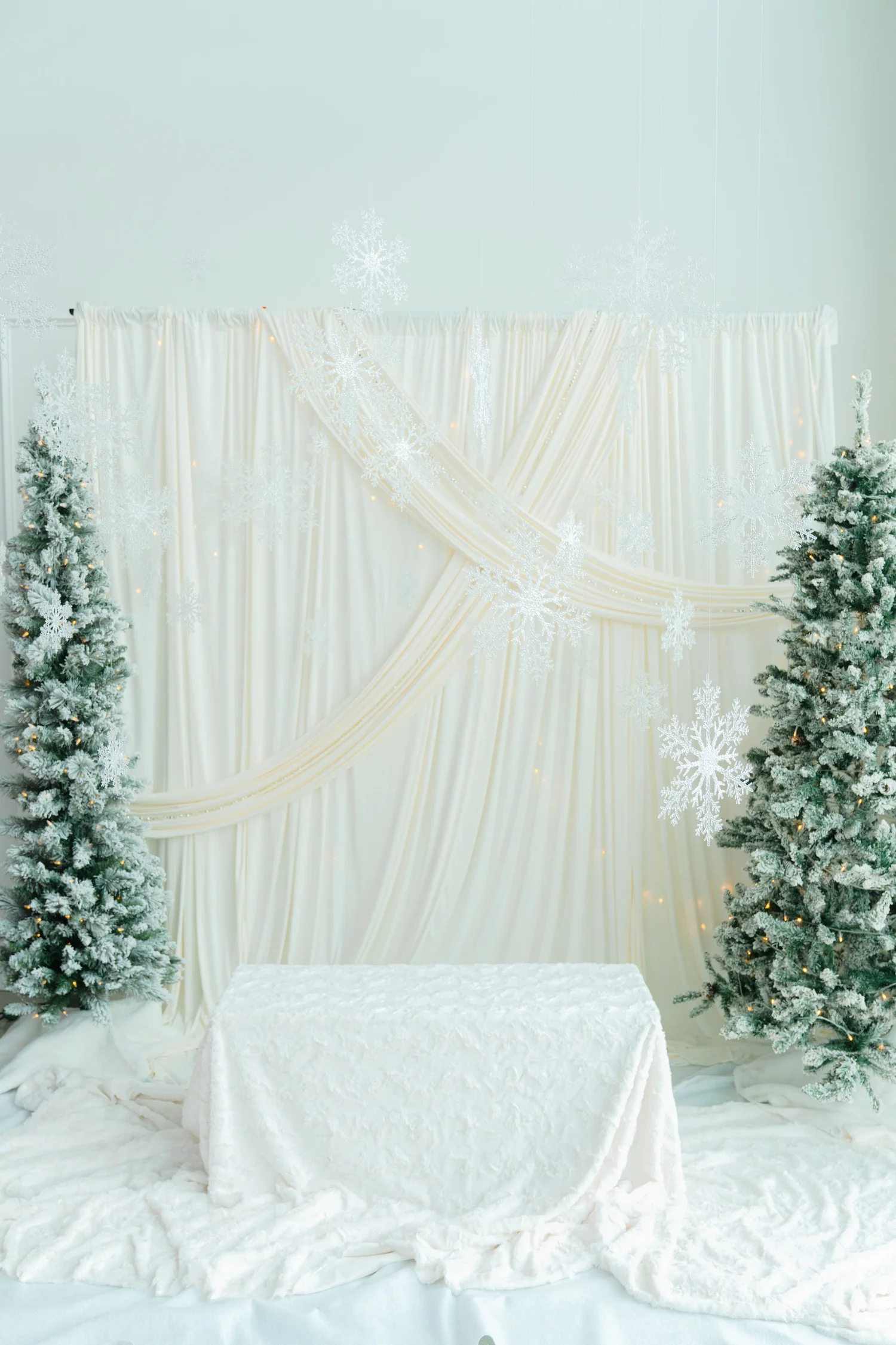 Full Winter White holiday photo set with ivory swag drapes, two frosted Christmas trees, hanging snowflakes and a faux fur bench at Alight Collaborative in Pflugerville, near Austin TX
