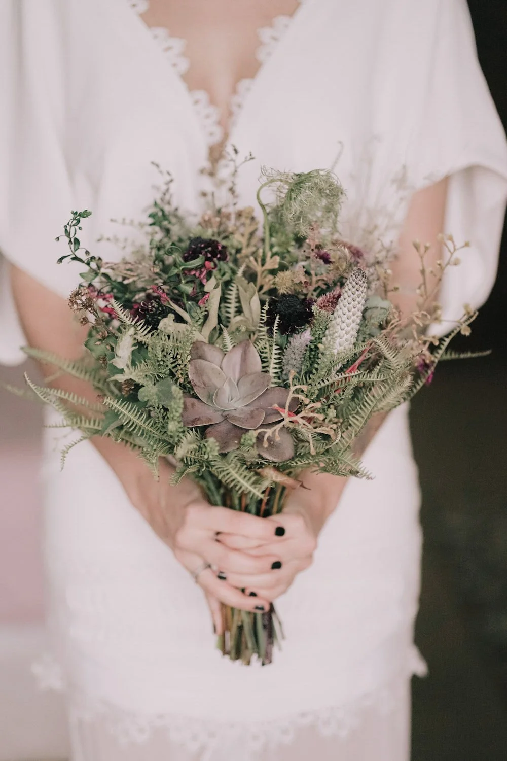 Vaso de flores com suculentas e plantas vermelhas, mulher com vestido branco ao fundo.