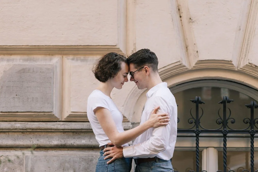 Casal apaixonado encostado na parede de um edifício antigo, sorrindo e com a testa tocando.