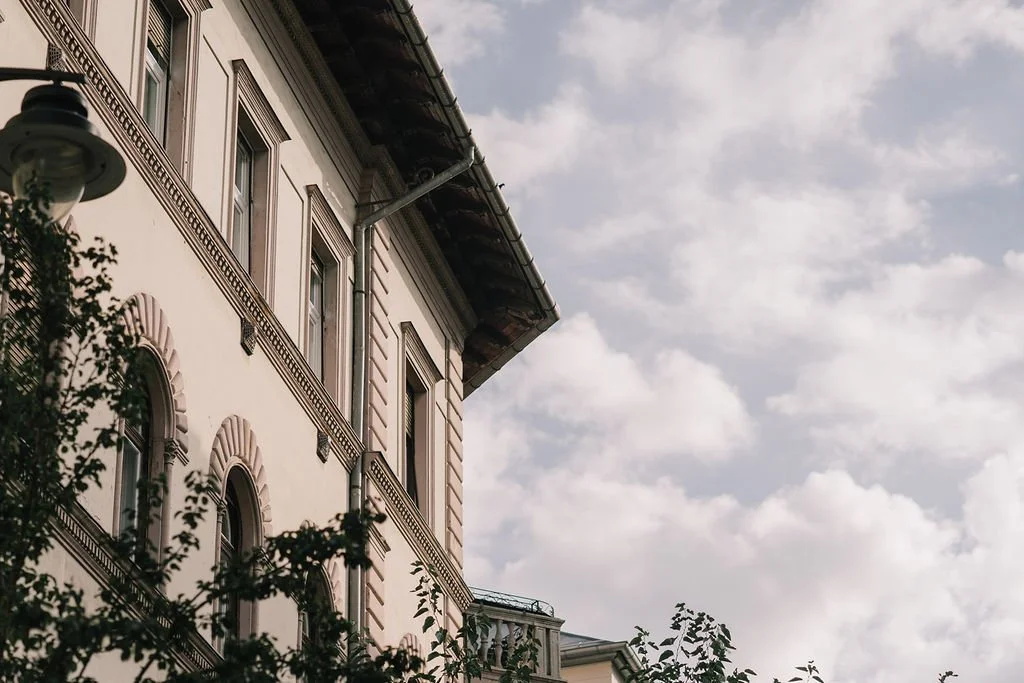 Fachada de um prédio antigo com janelas altas e detalhes arquitetônicos, visto parcialmente sob um céu nublado.