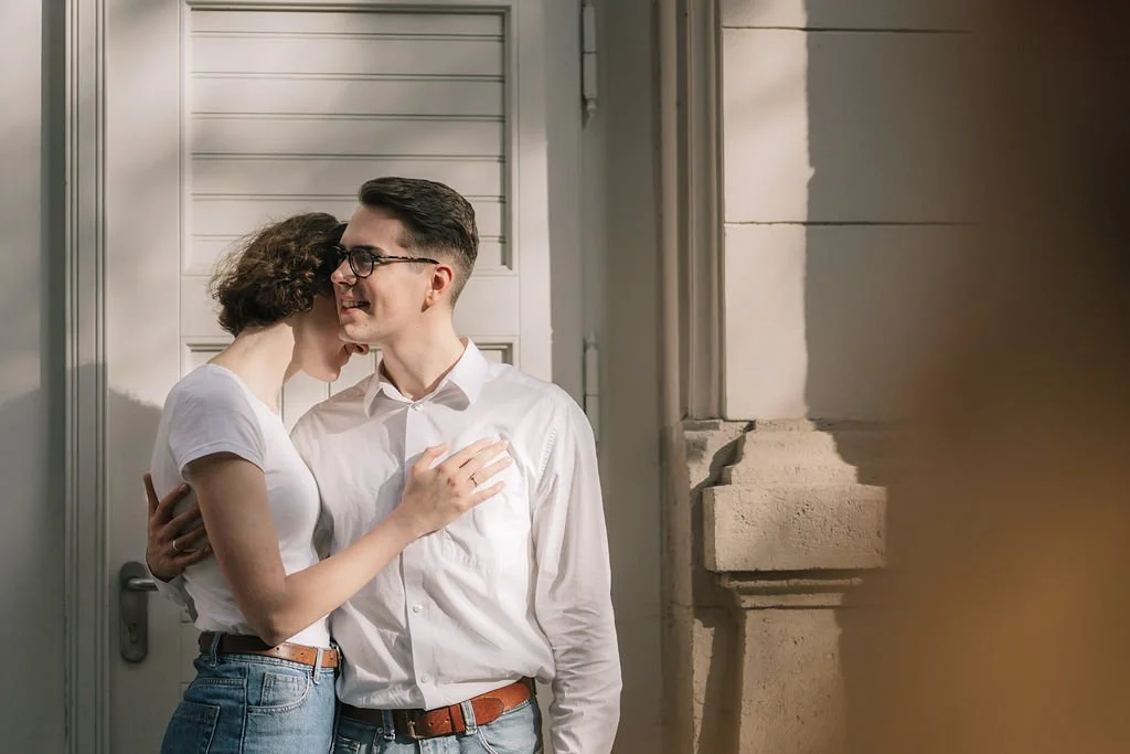 Casal de jovens sorrindo e abraçando-se em frente à porta de uma casa.