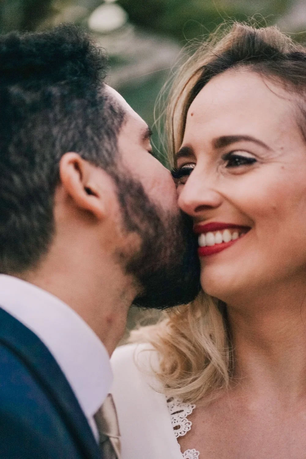 Casal sorrindo em close-up, prestes a se beijar, ao ar livre.