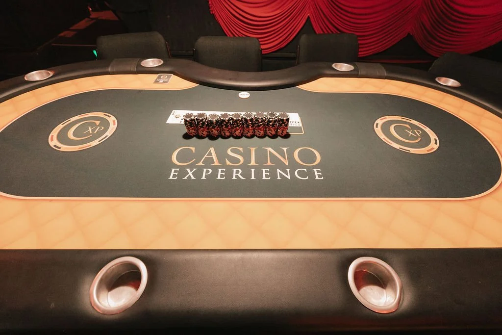 Mesa de pôquer no cassino com fichas empilhadas ao centro e cadeiras ao redor, com cortinas vermelhas ao fundo.