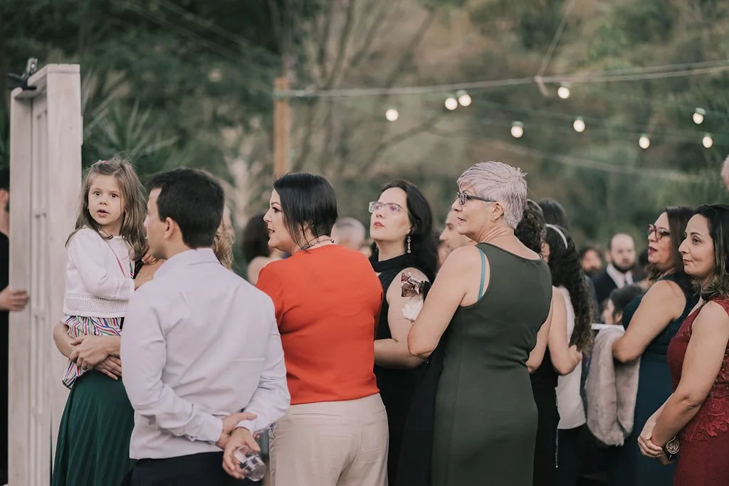 Grupo de pessoas se reunindo ao ar livre, algumas conversando, um menino e uma menina em destaque no centro.