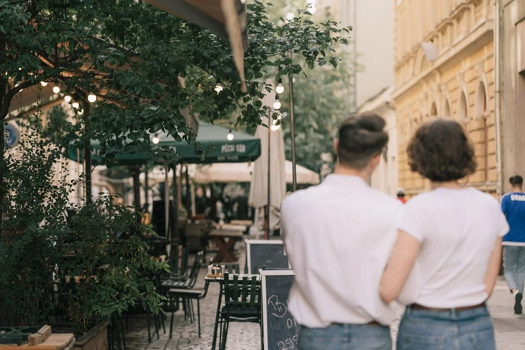 Casal caminhando pela rua de café ao ar livre com vegetação e iluminação decorativa.