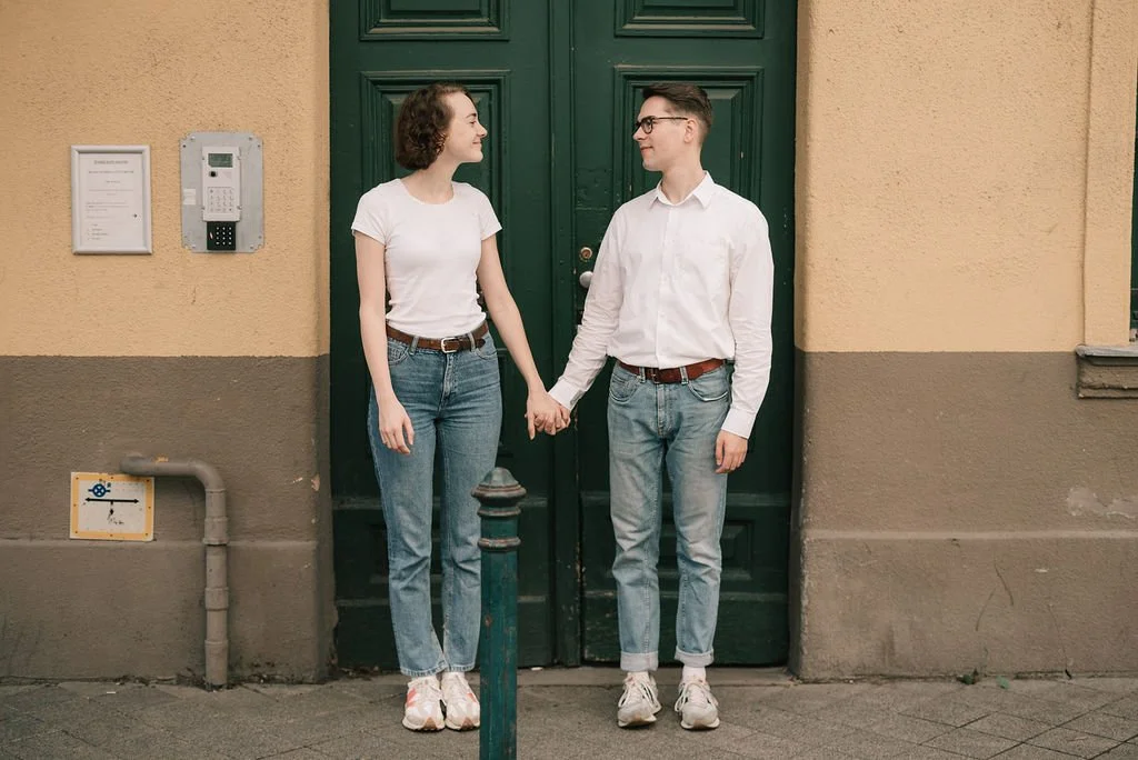 Casal jovem segurando as mãos em frente a uma porta de cor verde na rua