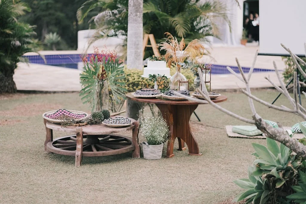Decoração ao ar livre com mesas de madeira, plantas e objetos decorativos, próximo a uma piscina.
