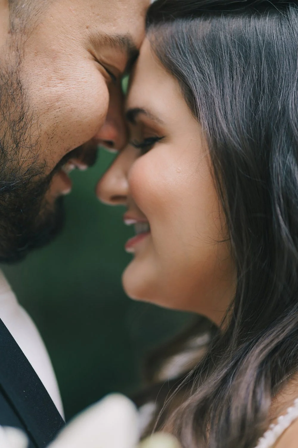 Casal sorridente com testa encostada, em close, com olhos fechados, em clima de amor.