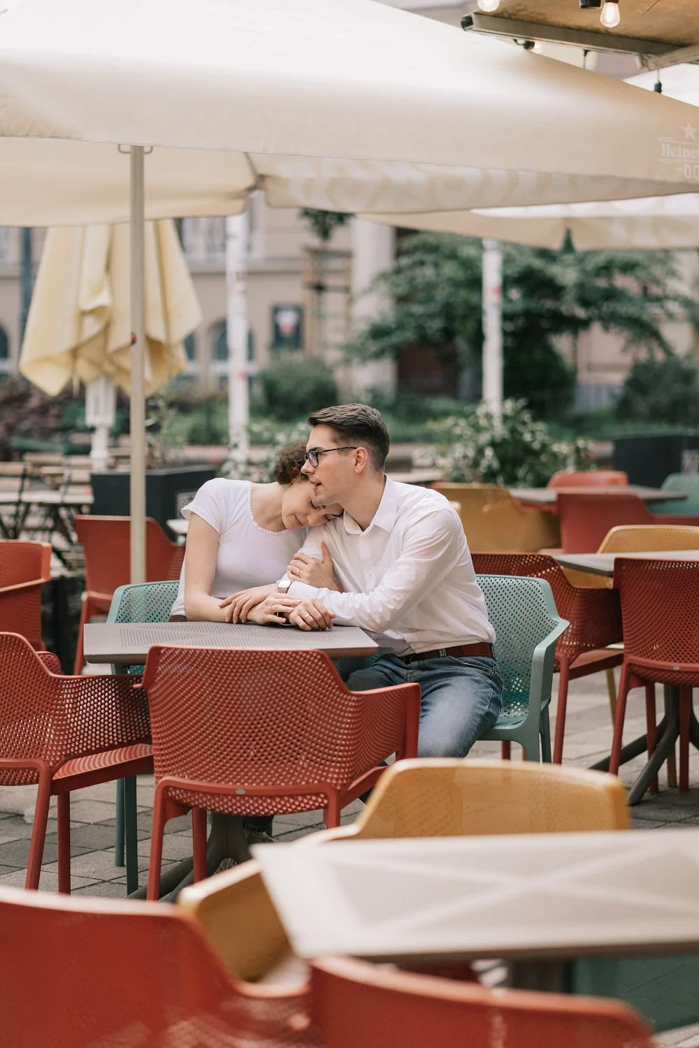 Casal apaixonado sentado em um restaurante ao ar livre, compartilhando um momento de ternura sob sombrinhas.