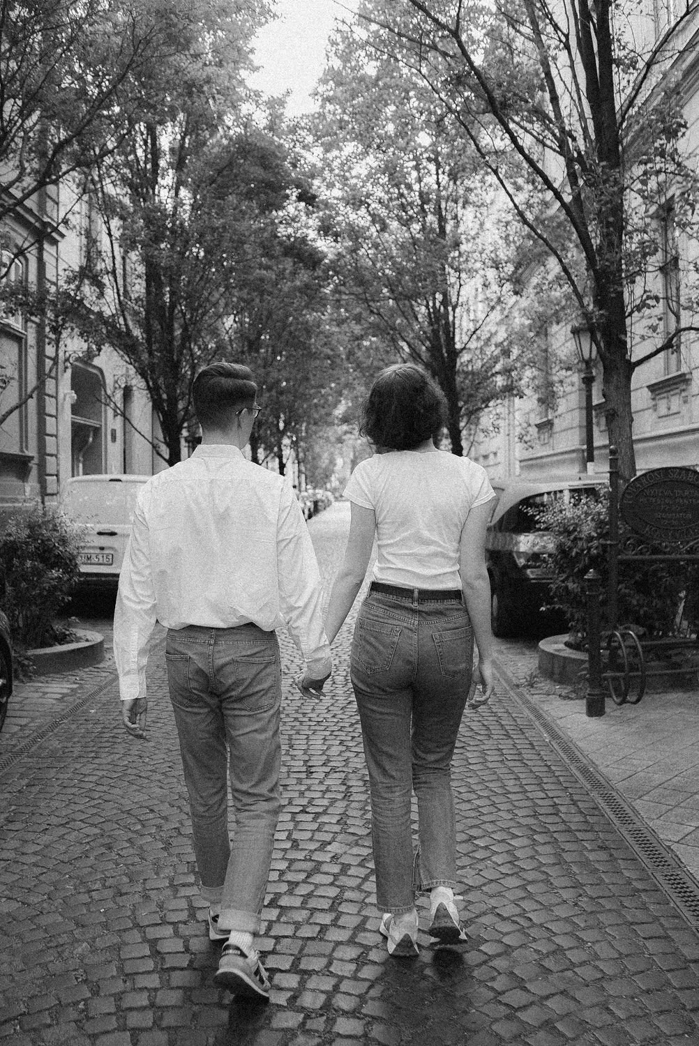 Casal andando de mãos dadas por uma rua de paralelepípedos em uma cidade.