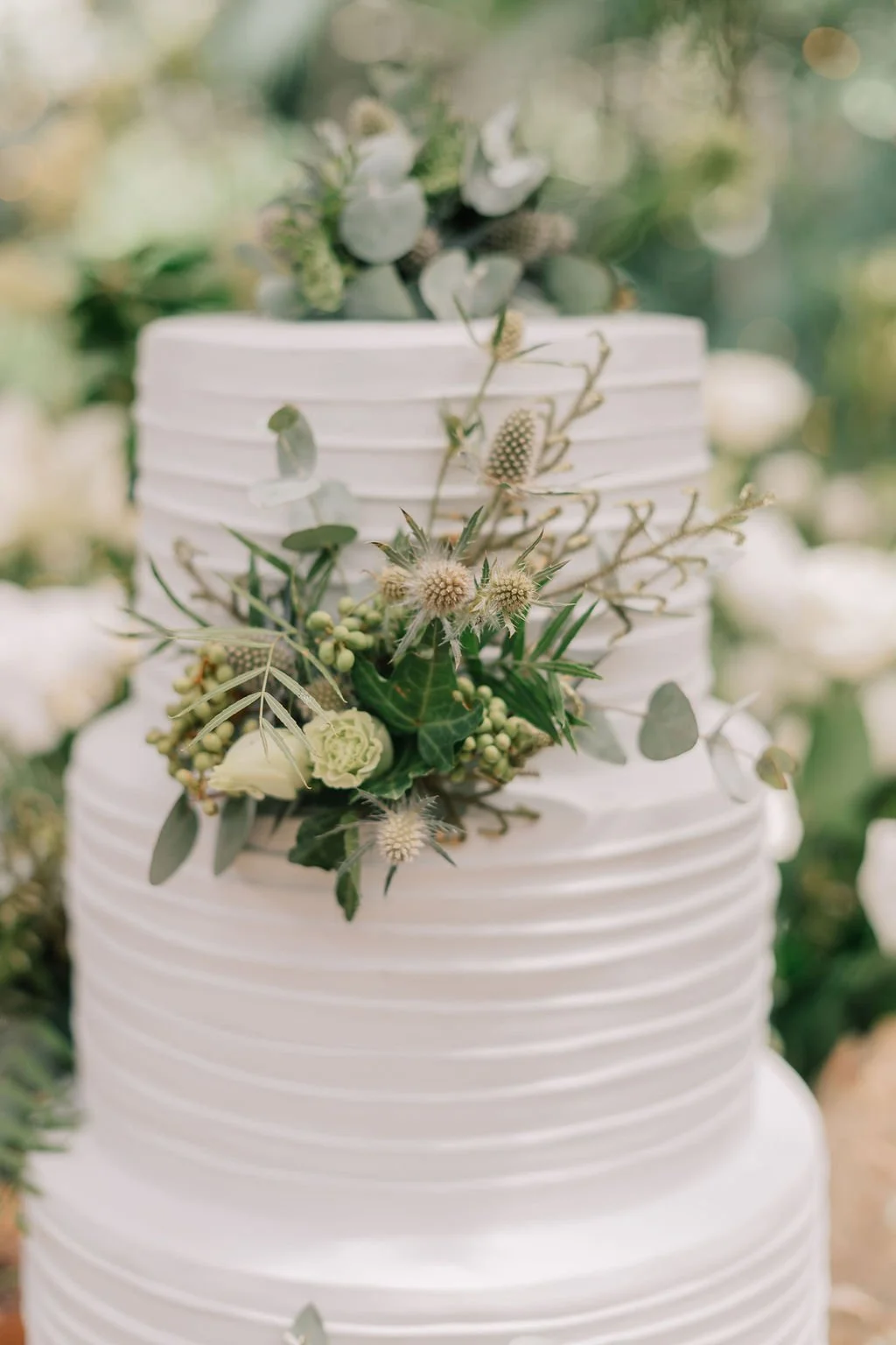 Bolo de casamento branco decorado com flores verdes e folhagens.