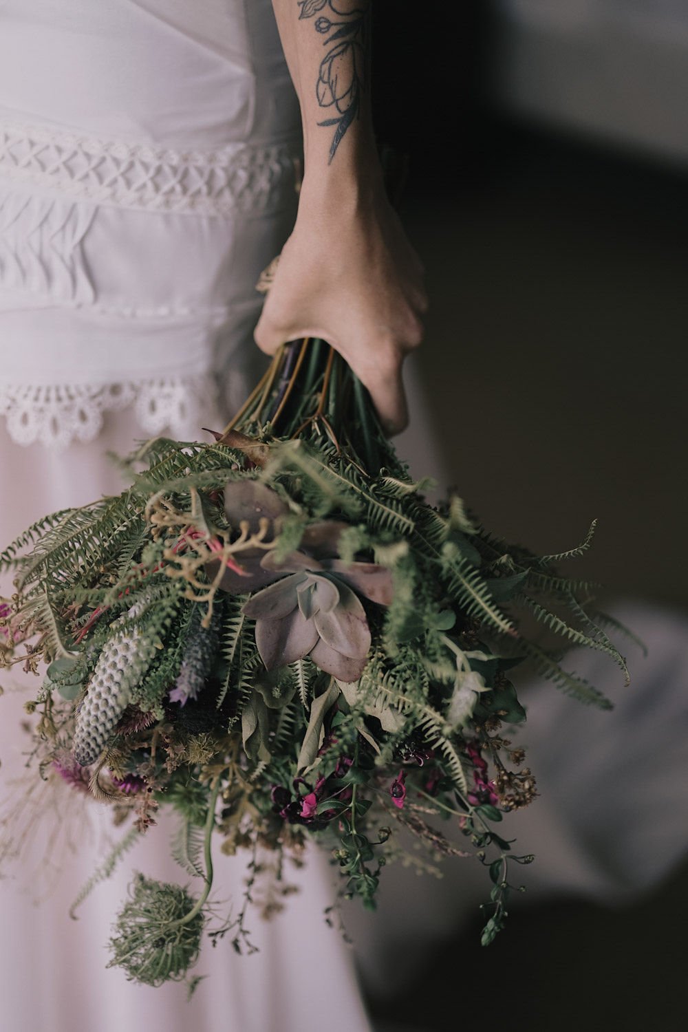 Pessoa segurando um buquê de flores junto ao vestido branco com detalhes em renda.