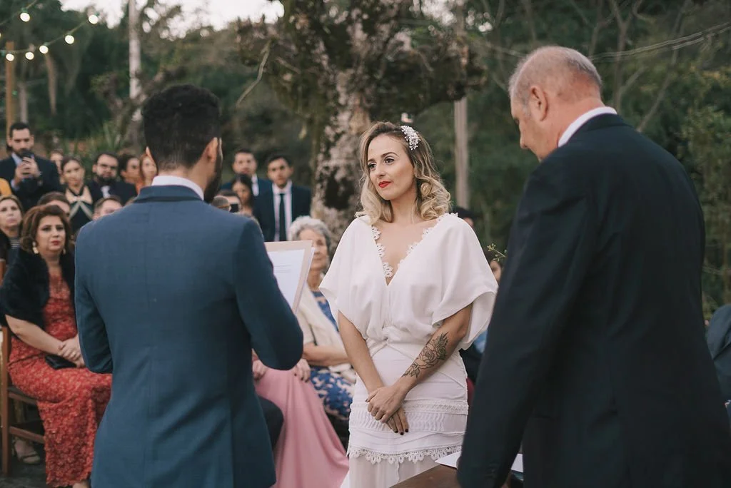 Casais trocando votos em casamento ao ar livre, com convidados assistindo.