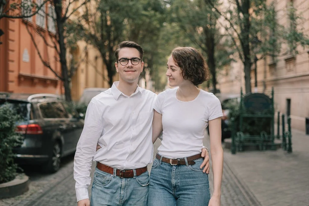 Jovens caminhando na rua, sorrindo, com árvores e edifícios ao fundo.