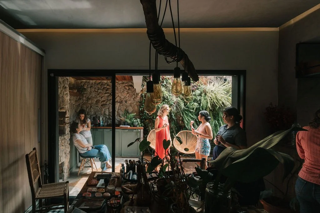 Grupo de mulheres conversando na varanda de uma casa com jardim, enquanto uma pessoa ao lado está sentada e uma outra está na cozinha ao fundo.