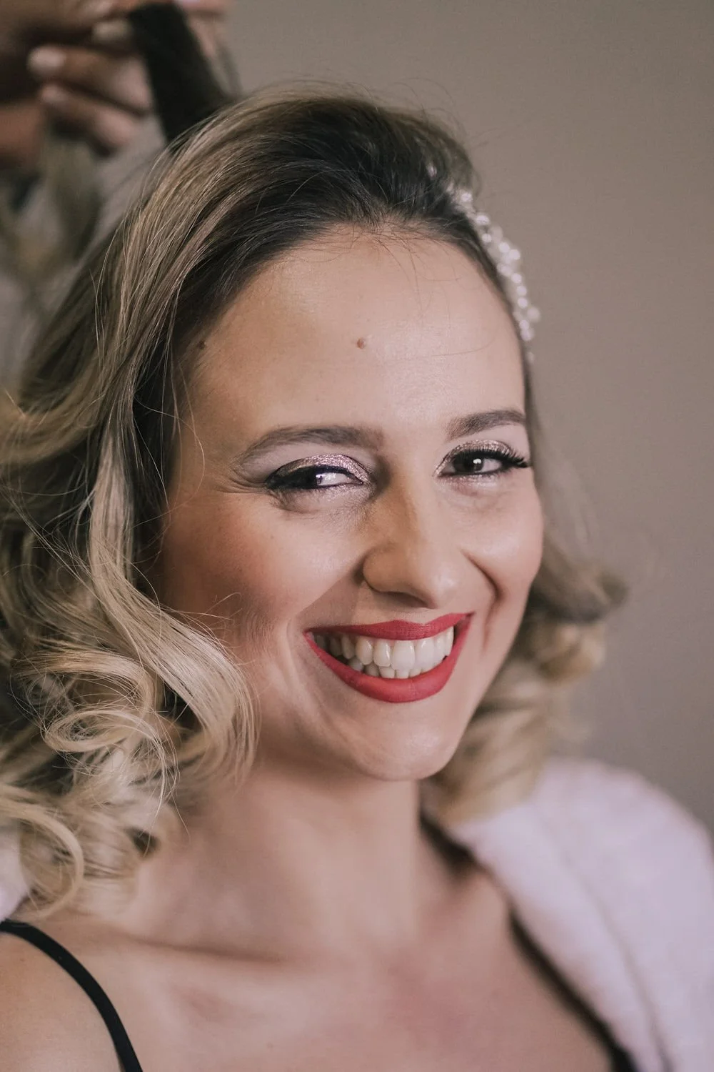 Mulher sorrindo com cabelo cacheado, maquiagem brilhante, lábios vermelhos e olhos de gatinho