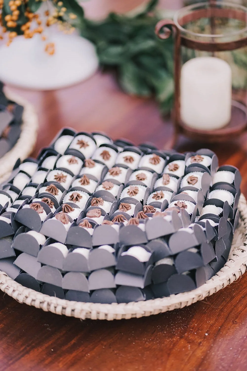 Docinhos decorados com cobertura de chocolate em uma bandeja de rolling pin, com decoração de plantas, vela e objeto de ferro ao fundo