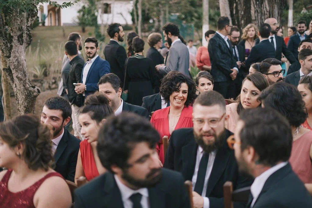 Pessoas em cerimônia ao ar livre, vestidas formalmente, conversando e sorrindo.