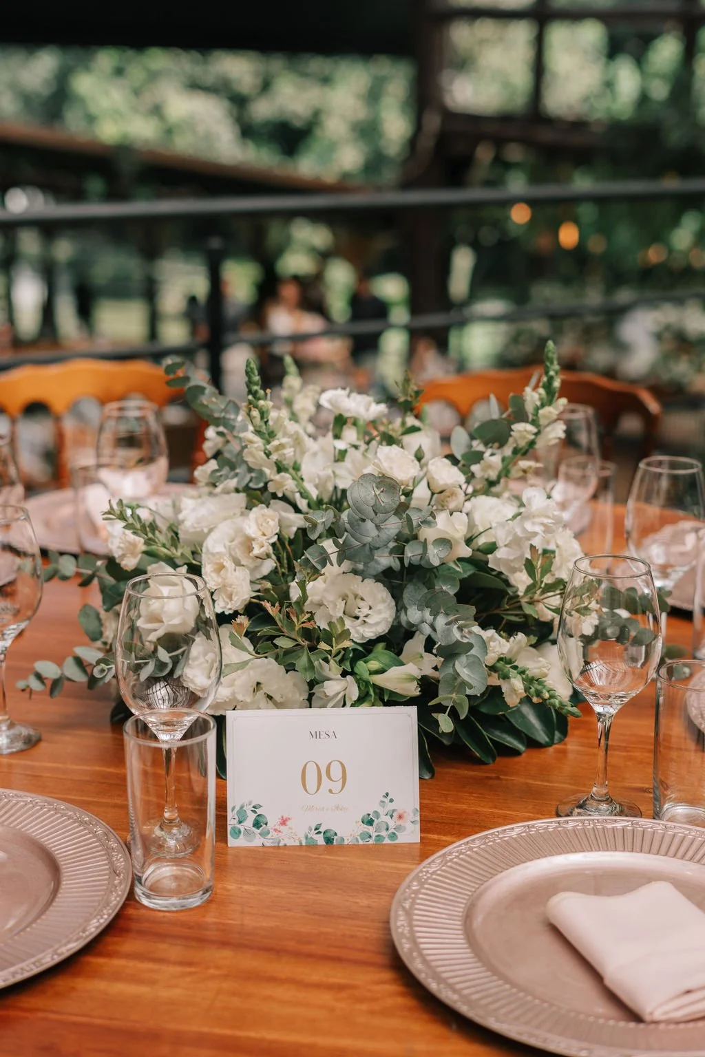 Mesa de casamento decorada com arranjo de flores brancas e taças de vidro, com número 09 no centro.