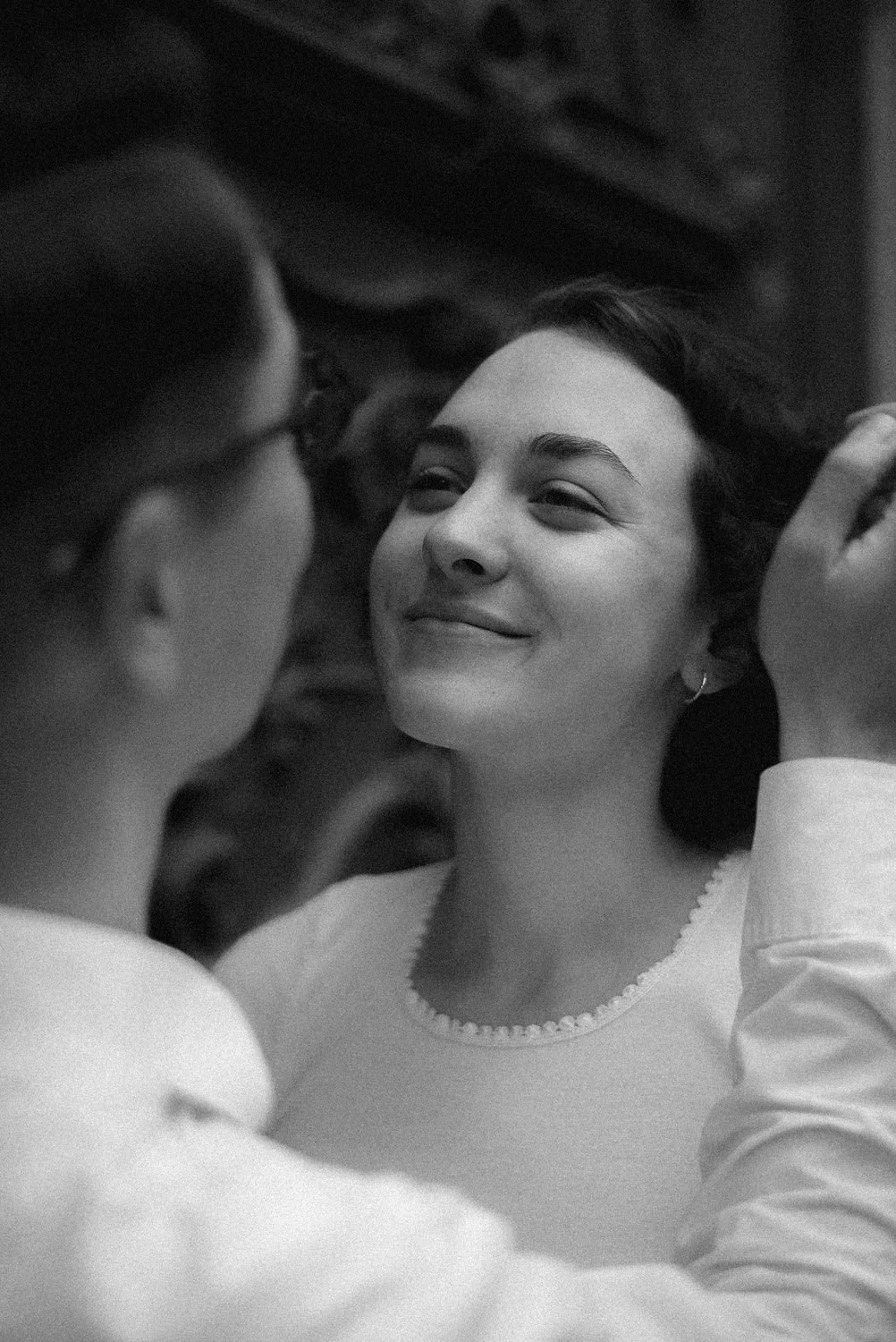 Mulher sorrindo com outra pessoa perto, em um momento íntimo, em preto e branco.