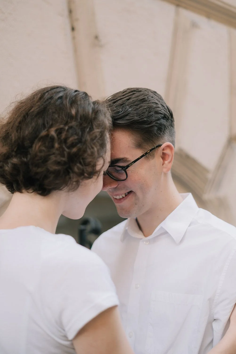 Casal sorridente com cabeças juntas, se olhando carinhosamente, em um momento íntimo, em um ambiente interno com teto de madeira.