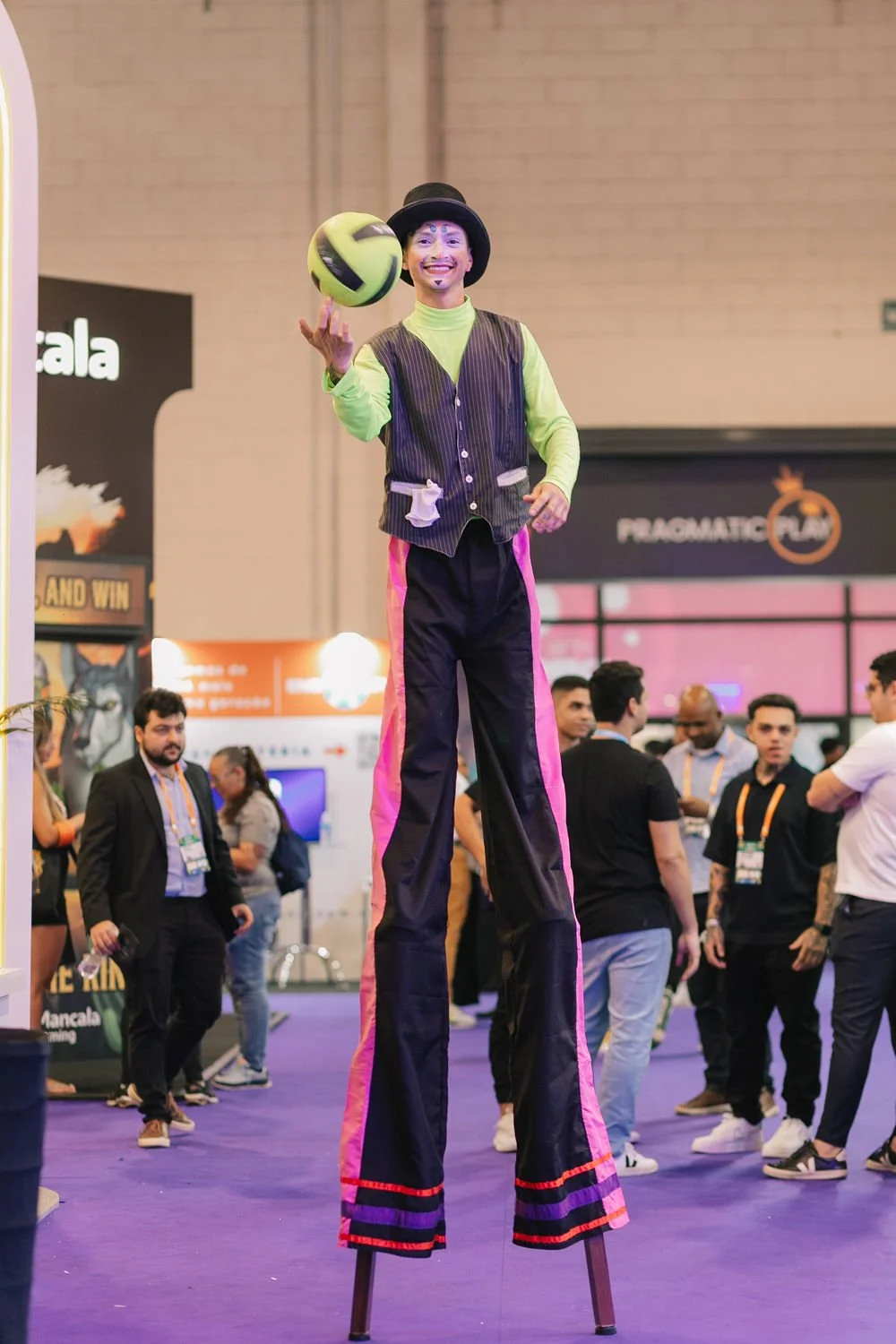 Palhaço em um espetáculo de rua, equilibrando-se em patas de um meio-fio, enquanto brinca com uma bola de futebol.