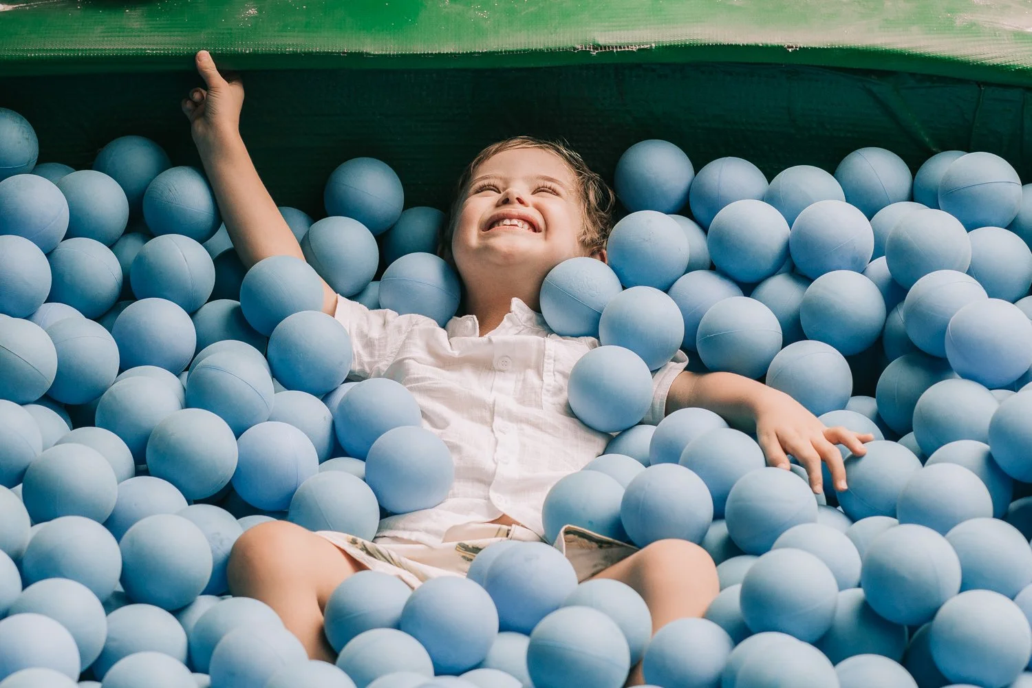 Menino sorrindo em uma piscina de bolas azul claro.