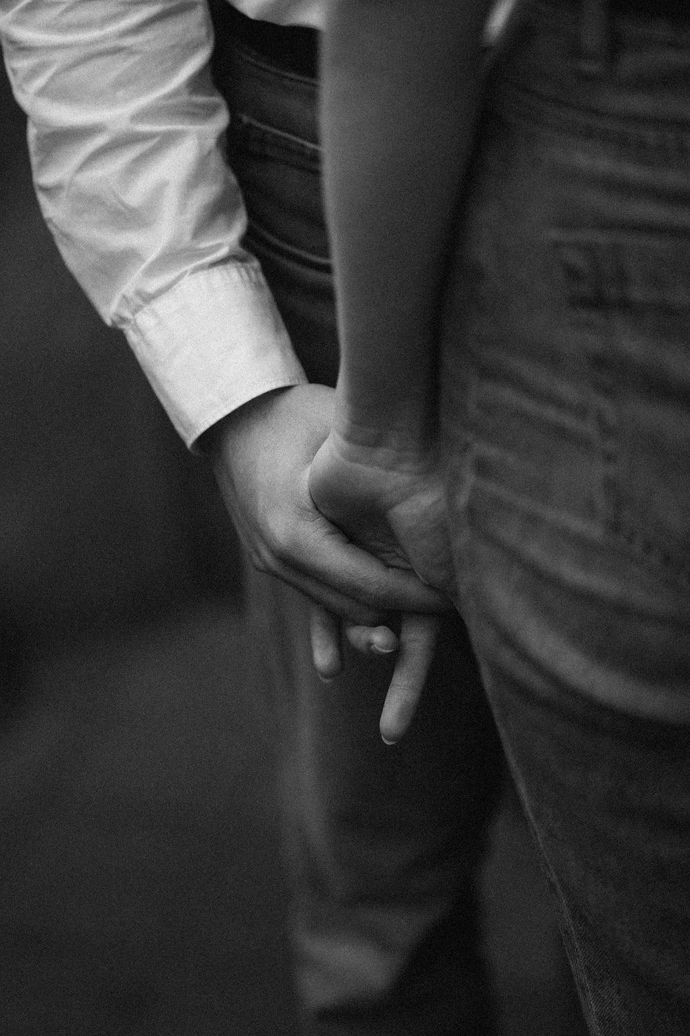 Imagem em preto e branco mostrando duas pessoas de mãos dadas, com uma delas usando uma camisa de manga longa e a outra de uma camiseta, numa cena próxima.