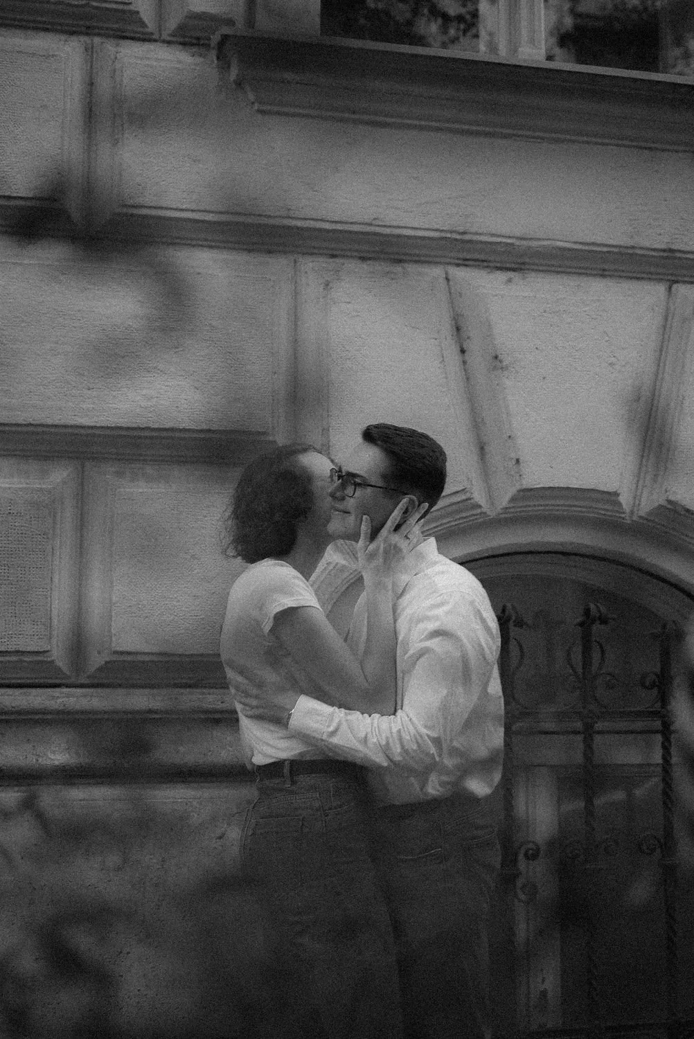 Um casal jovem se beijando em frente a uma parede de pedra ou concreto.