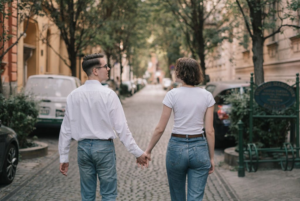Casal caminhando de mãos dadas em rua arborizada