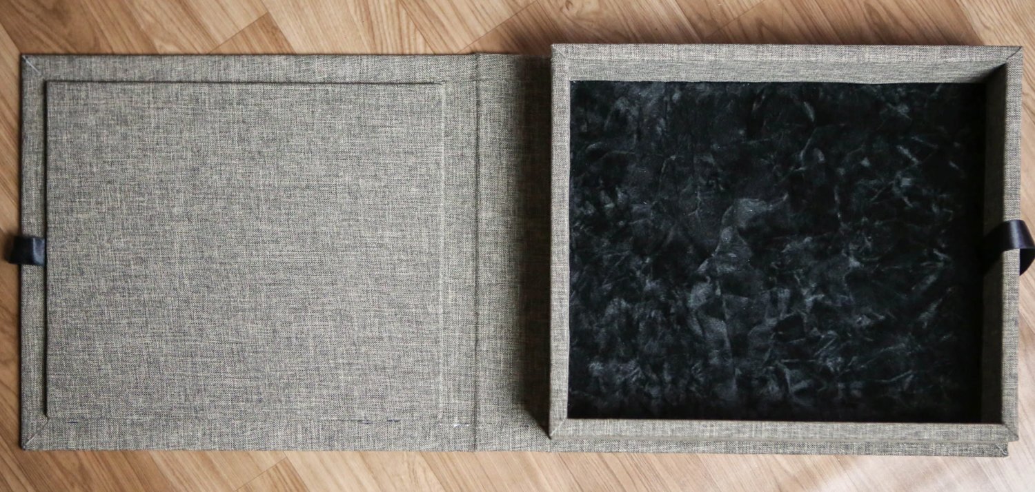 Open gray fabric-covered box on wooden floor, with textured black interior.