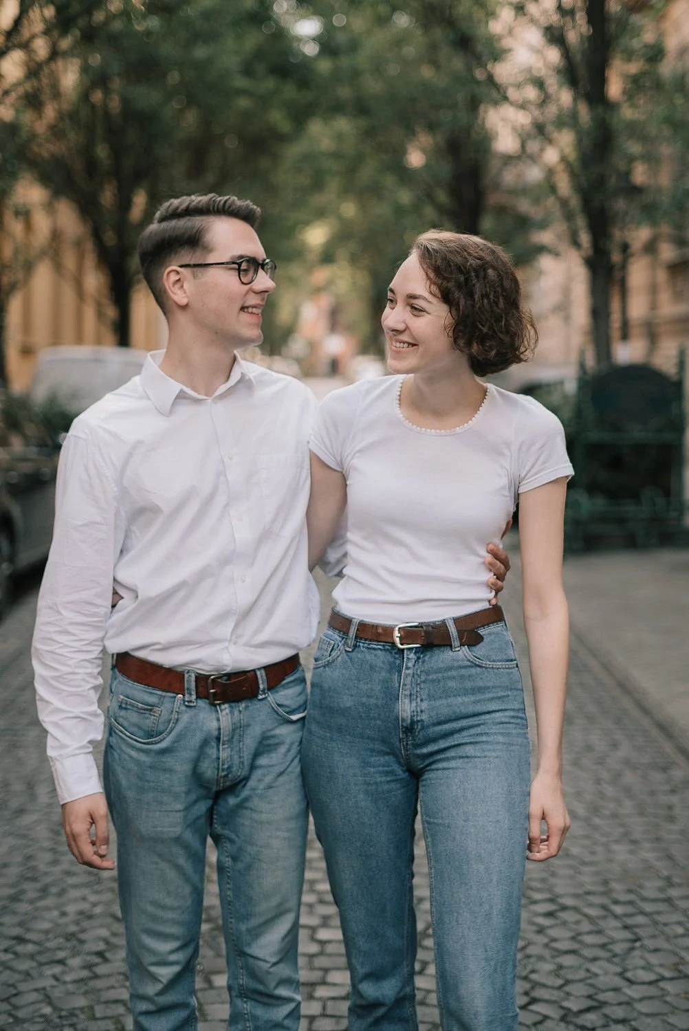 Homens e mulher caminhando juntos na rua, sorrindo, com árvores ao fundo.