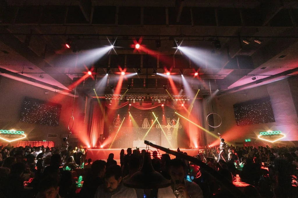 Cena de um grande espetáculo ou show com iluminação colorida, palco com elementos geométricos e uma grande audiência.