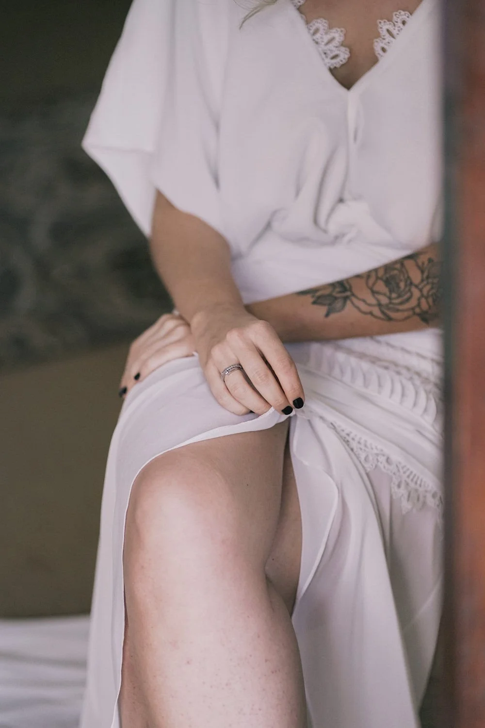 Pessoa usando roupa branca, com tatuagem de flor no braço, segurando a saia e mostrando a perna.