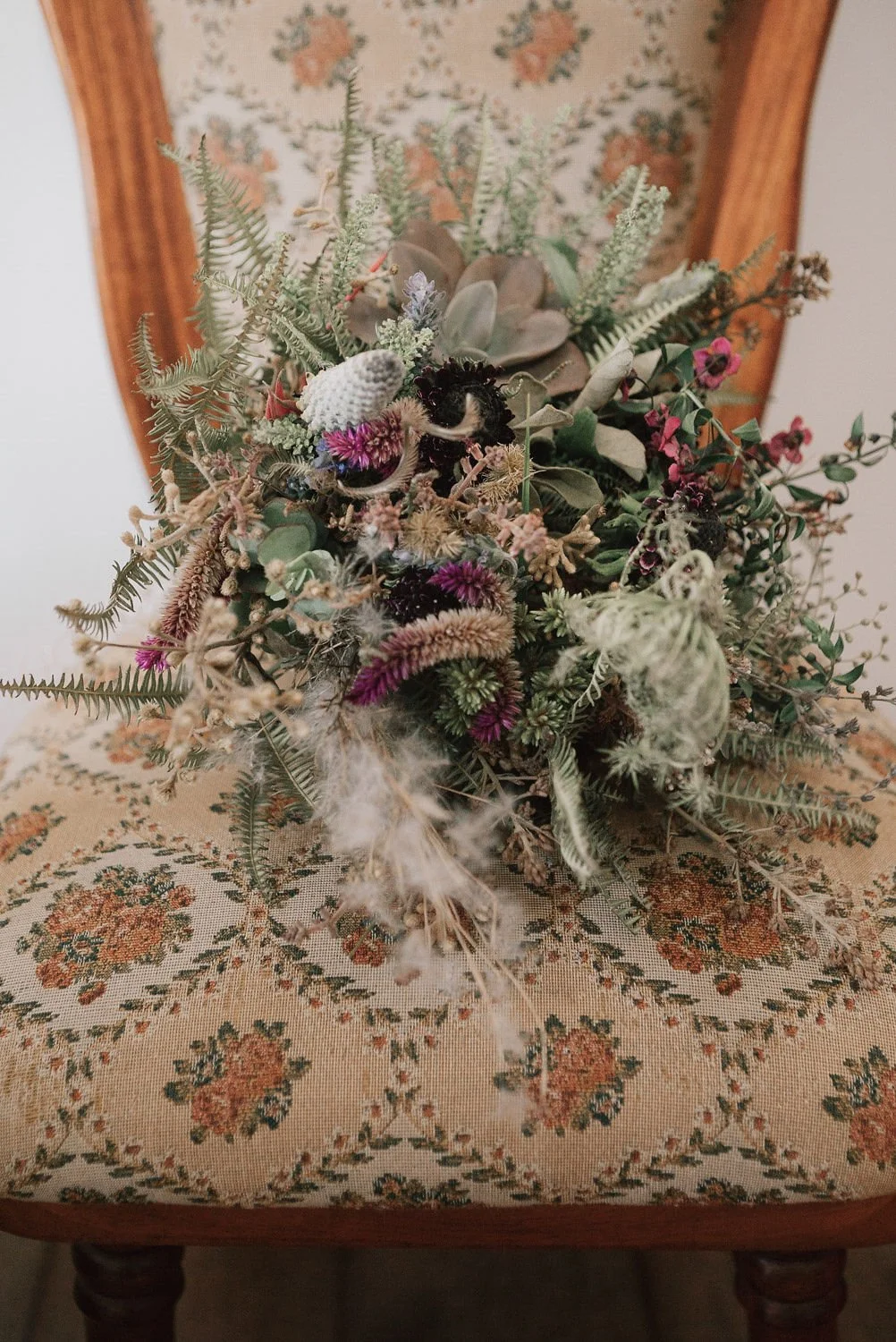 Arranjo de flores secas e plantas suculentas sobre uma cadeira de madeira encostada na parede.