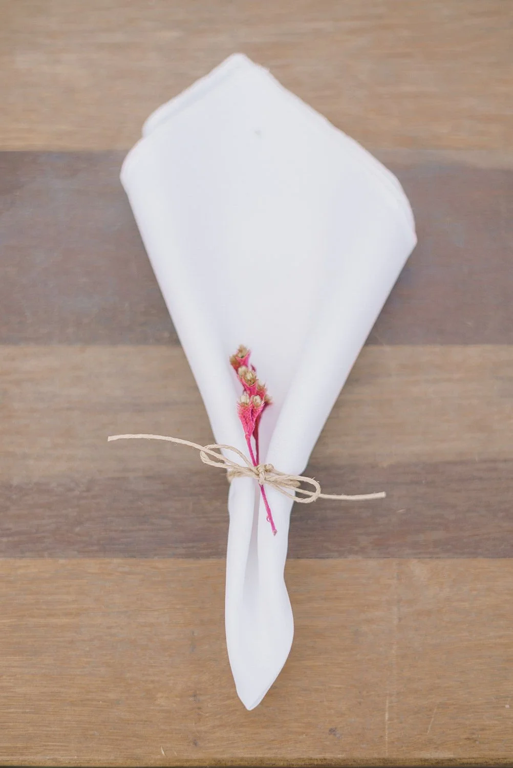 Dinosaurier-Figur in weißem Stoff, umwickelt mit einem pinken Band, auf einem Holztisch.