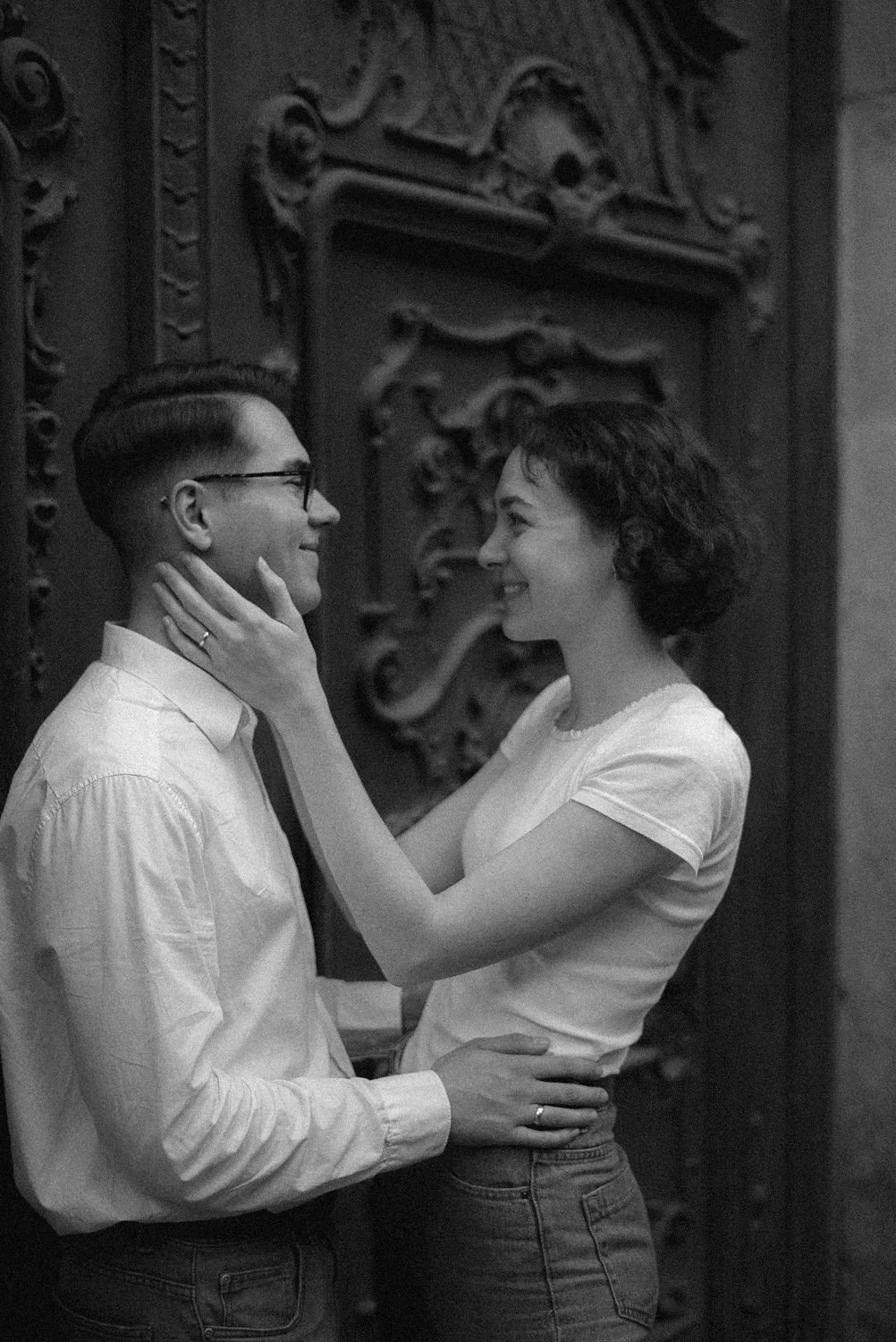 Homem e mulher olhando um nos olhos, sorrindo, com a mulher segurando o rosto do homem e a outra mão na cintura dele, em um cenário de cor diferentes em preto e branco.