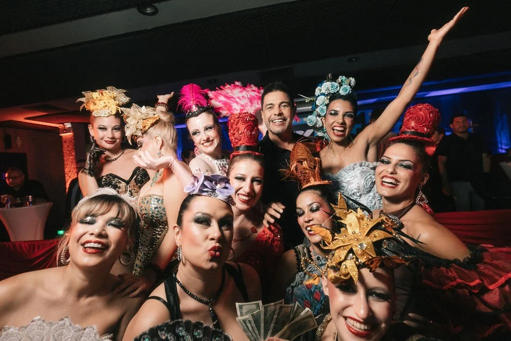 Grupo de pessoas vestindo roupas de baile em um evento festivo, com adereços coloridos e sorrindo para a câmera.