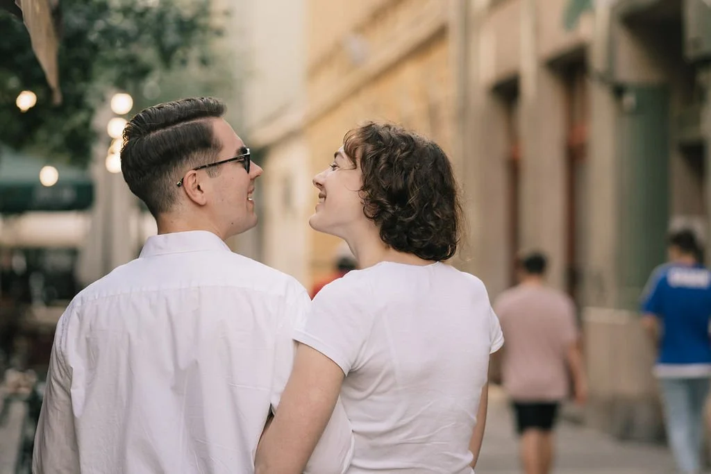 Casal sorridente caminhando de costas na rua durante o dia, cenário urbano ao fundo.