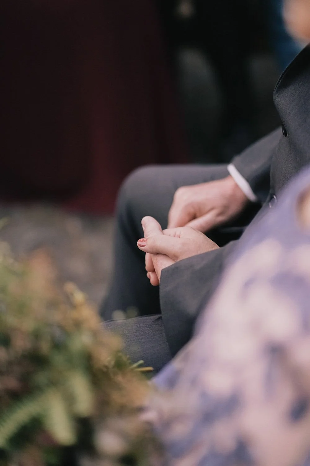 Pessoa usando terno, sentado, com mãos entrelaçadas, em um ambiente externo